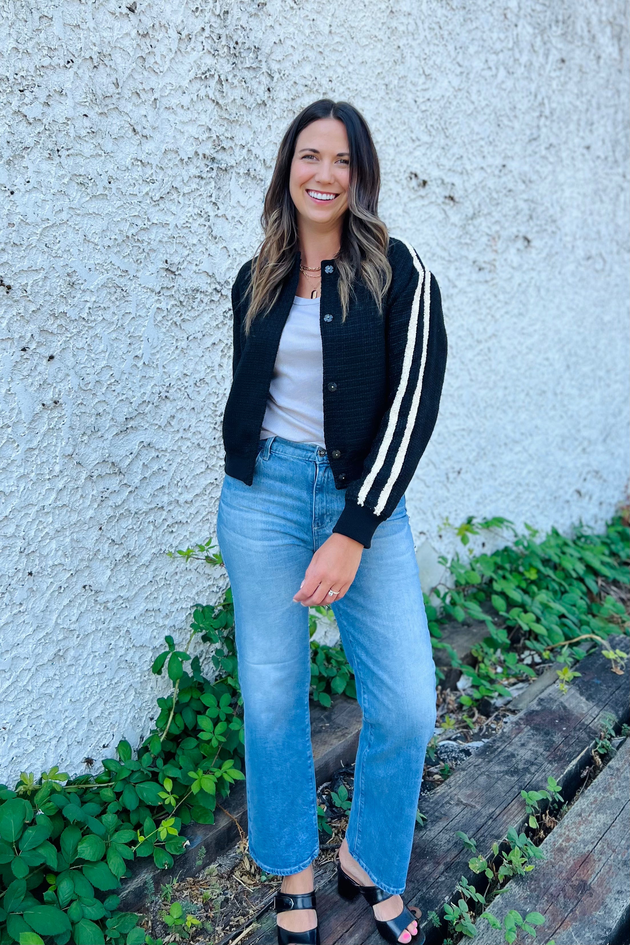 Woman wearing a black and white striped cardigan, white shirt, and blue jeans against a textured wall.