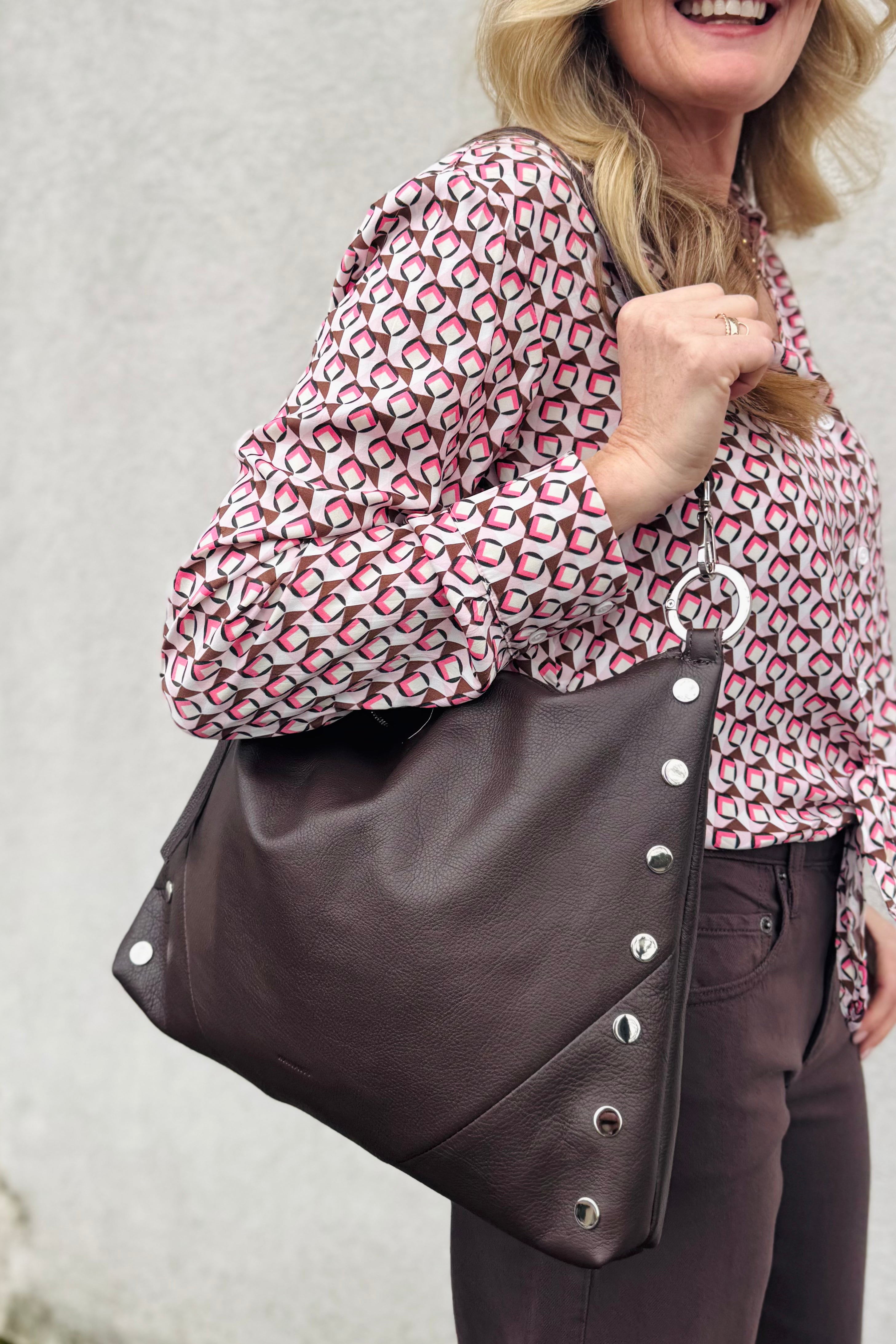 Woman holding a brown leather bag with silver studs. Perfect for this time of the year. great gift too
