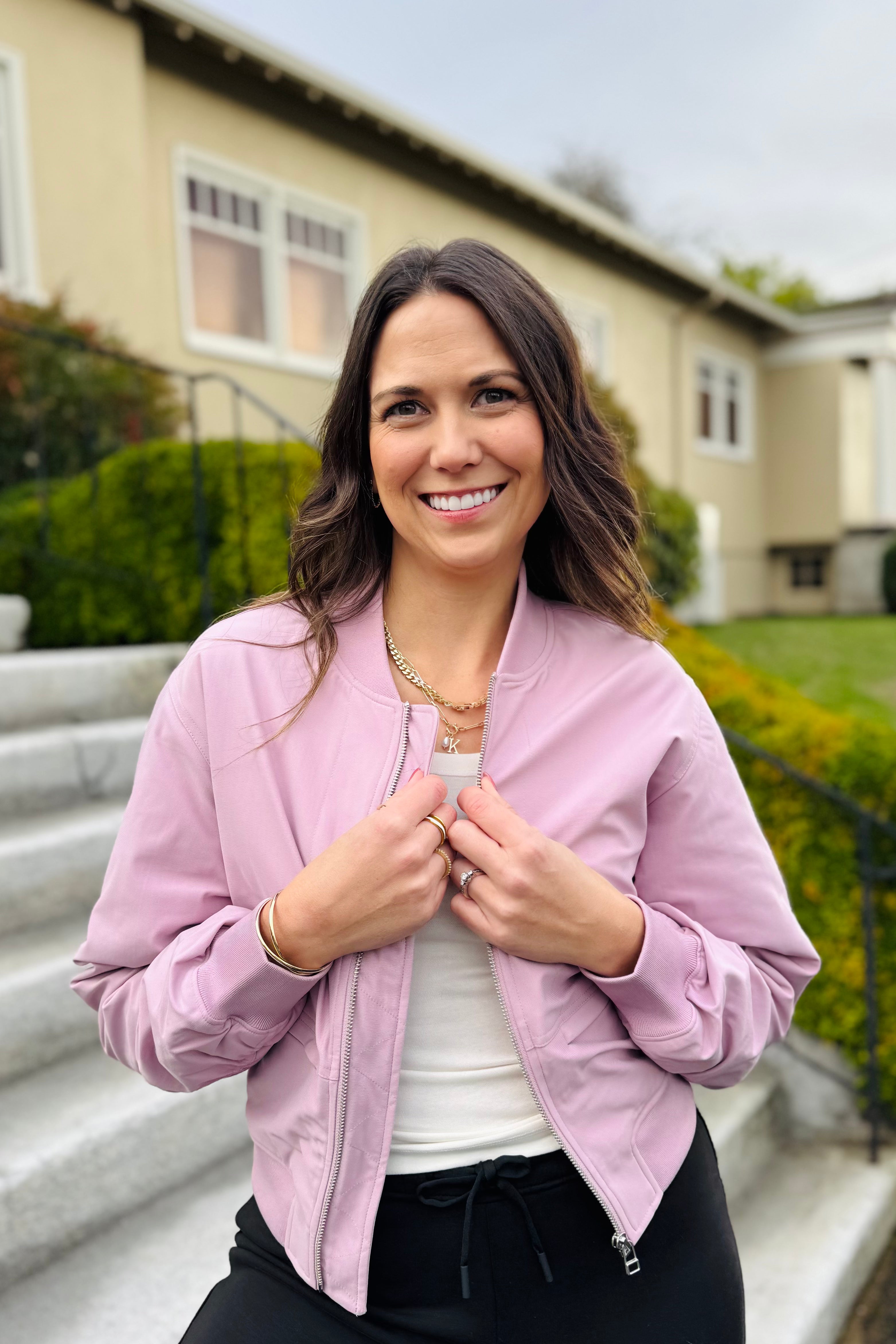 Woman in a pink jacket standing outdoors with a house in the background