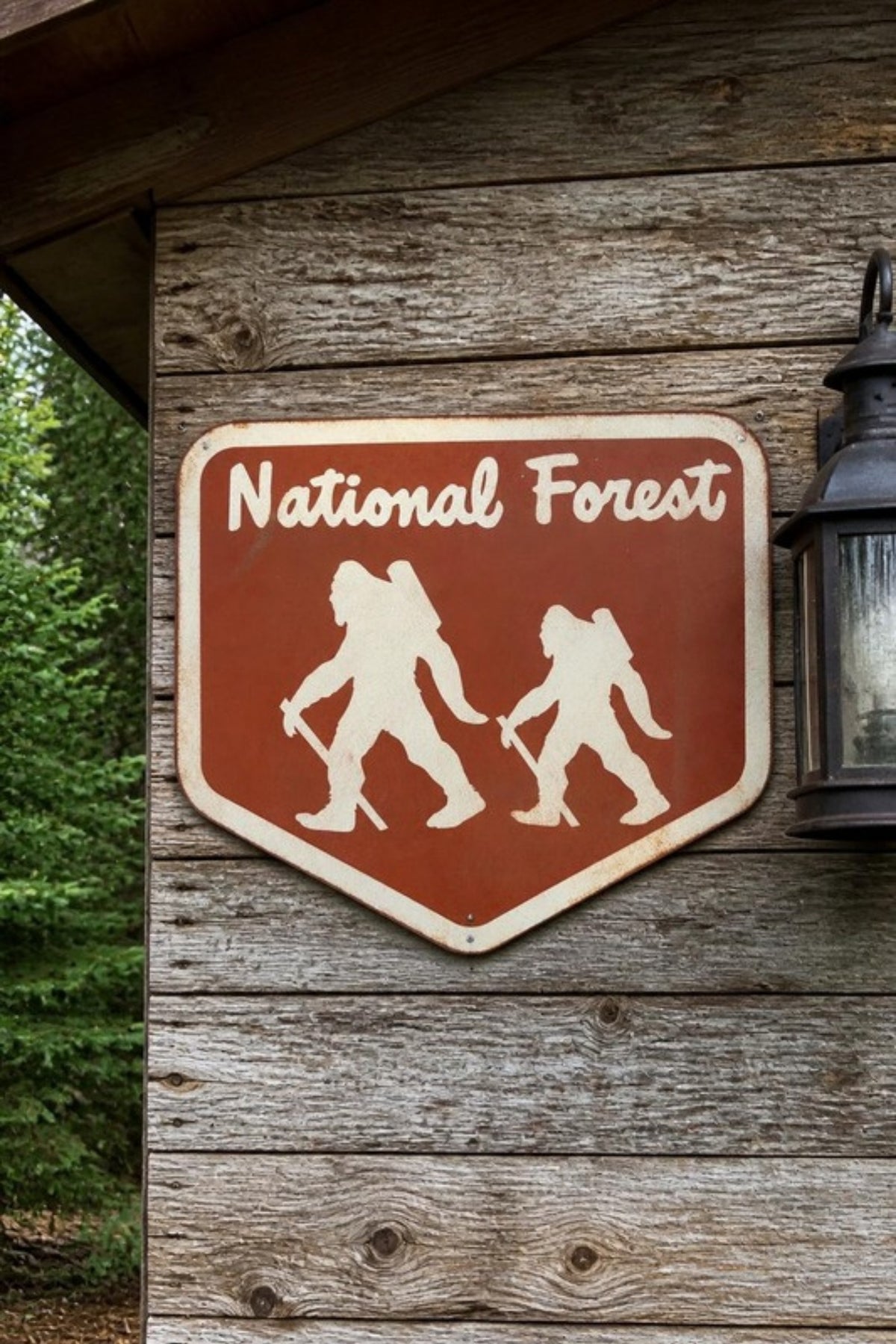 Fosterweld Bigfoot National Forest Adventure Sign in Autumn/Burnt Orange on a cabin porch, a handmade metal sign for the cabin, garage, porch or man cave, and a fun gift for Bigfoot fans