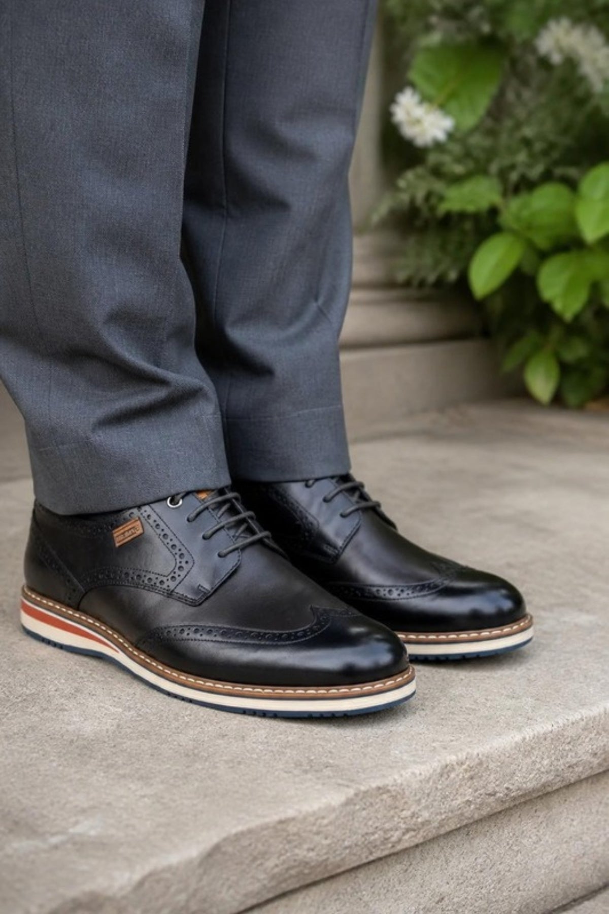 Pikolinos Avila dress shoe in Black leather with wingtip perforations and a contrast welt sole, worn with grey dress trousers on stone steps, an elegant, comfortable lace-up for weddings, the office, date nights and dressing up dark jeans