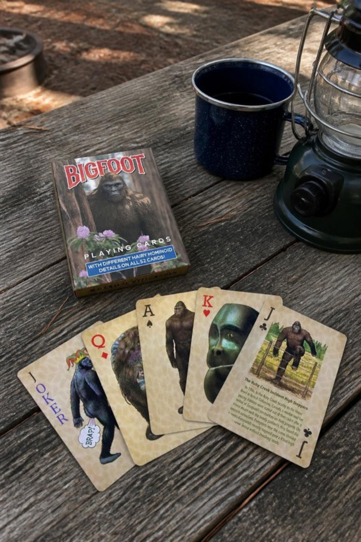 Paradise Cay Publications Bigfoot playing cards on a campsite picnic table, a 52-card deck with different Bigfoot art on every card for camping trips, cabin weekends and game nights, and a fun stocking stuffer