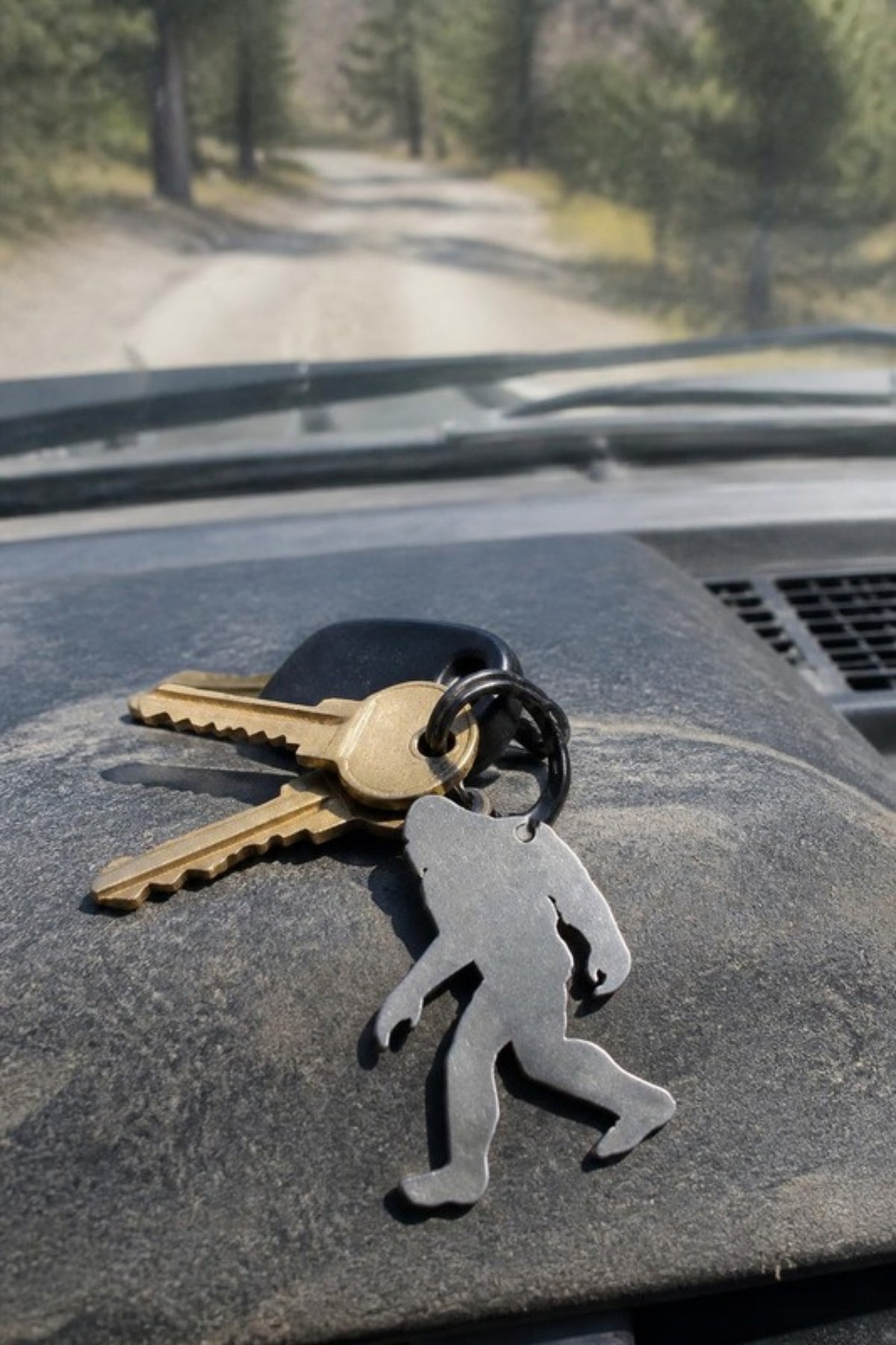 Paradise Cay Publications Bigfoot walking keychain with truck keys on a dashboard, a stainless steel Bigfoot keychain and bottle opener for everyday carry, road trips and camping, and a great small gift