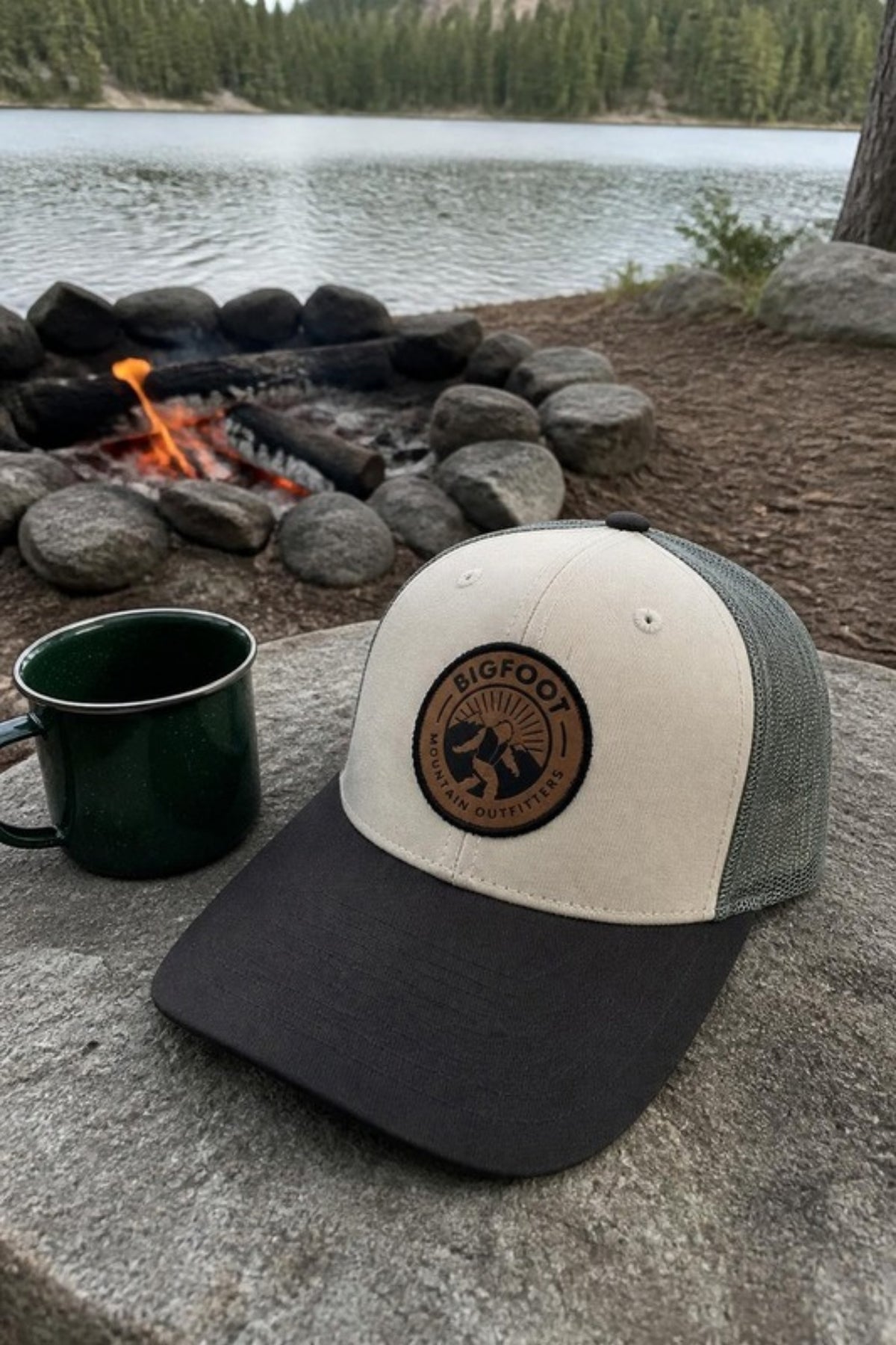 Bigfoot Mountain Outfitters BMO Mesh Hat in Loden/Tan by the campfire at a lakeside campsite, a leather-patch trucker hat for camping trips, lake days and everyday wear