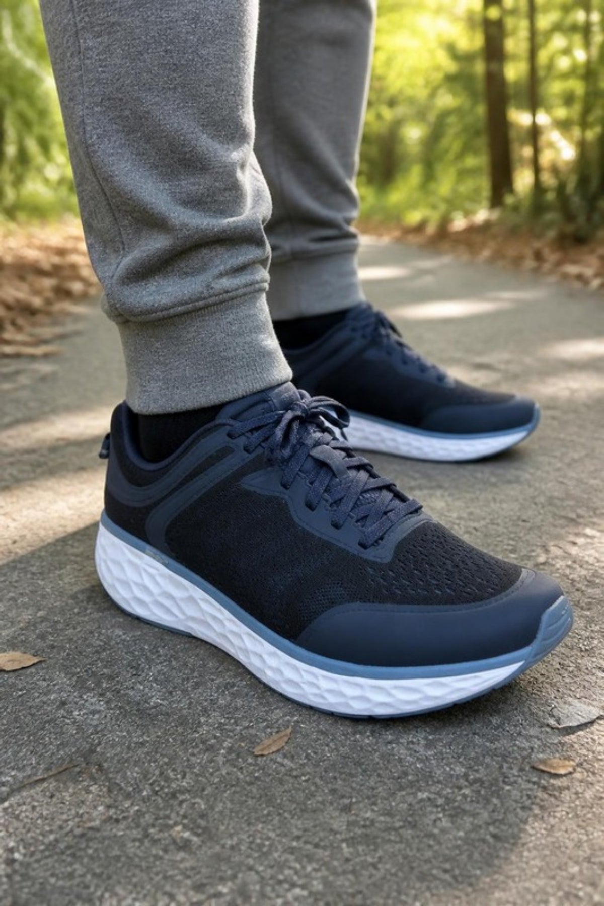 Aetrex Chase sneaker in Navy mesh with a thick white UltraSKY cushioned sole, worn with grey joggers on a leafy park path, a supportive arch-support walking shoe for long walks, travel days, errands and standing all day