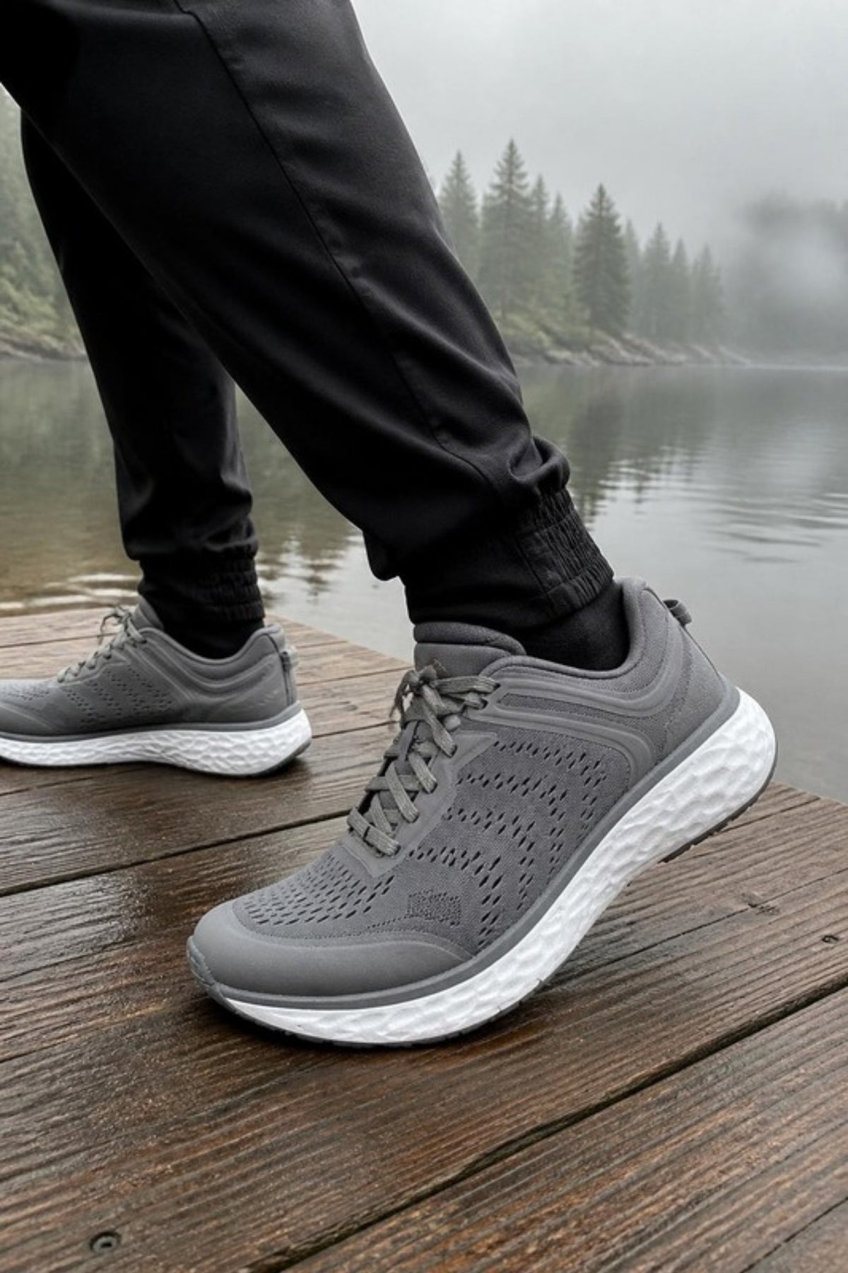 Aetrex Chase sneaker in Silver grey perforated mesh with a thick white cushioned sole, worn with black joggers on a lakeside dock, a supportive, machine-washable walking sneaker for morning walks, travel, gym days and all-day comfort on your feet