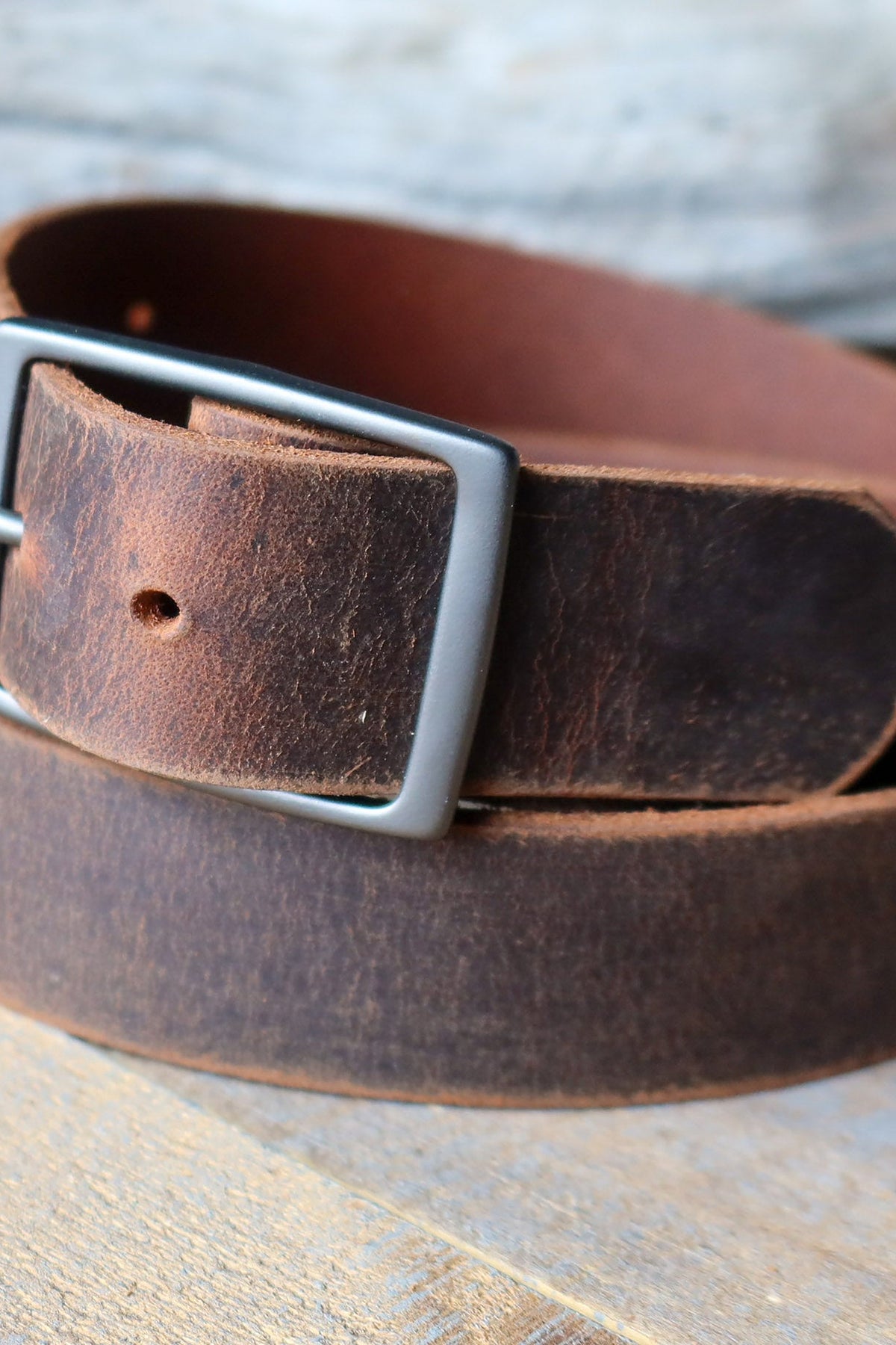 Fosterweld Crazy Horse Leather Belt in Brown close up on weathered wood, showing the rich distressed patina and brushed buckle, a rugged everyday belt and great gift