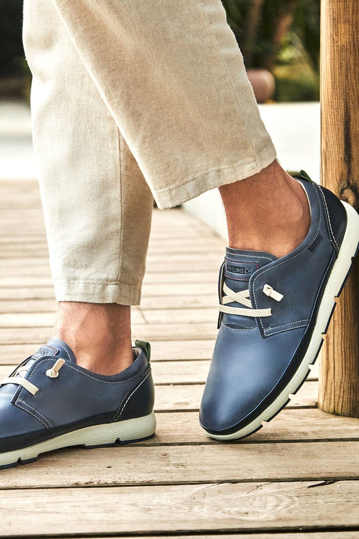 Pikolinos Fuencarral Shoe in Pacific navy leather with toggle laces, worn with linen trousers on a wooden boardwalk, a lightweight casual lace-up for summer travel, weekend strolls, the office and seaside dinners