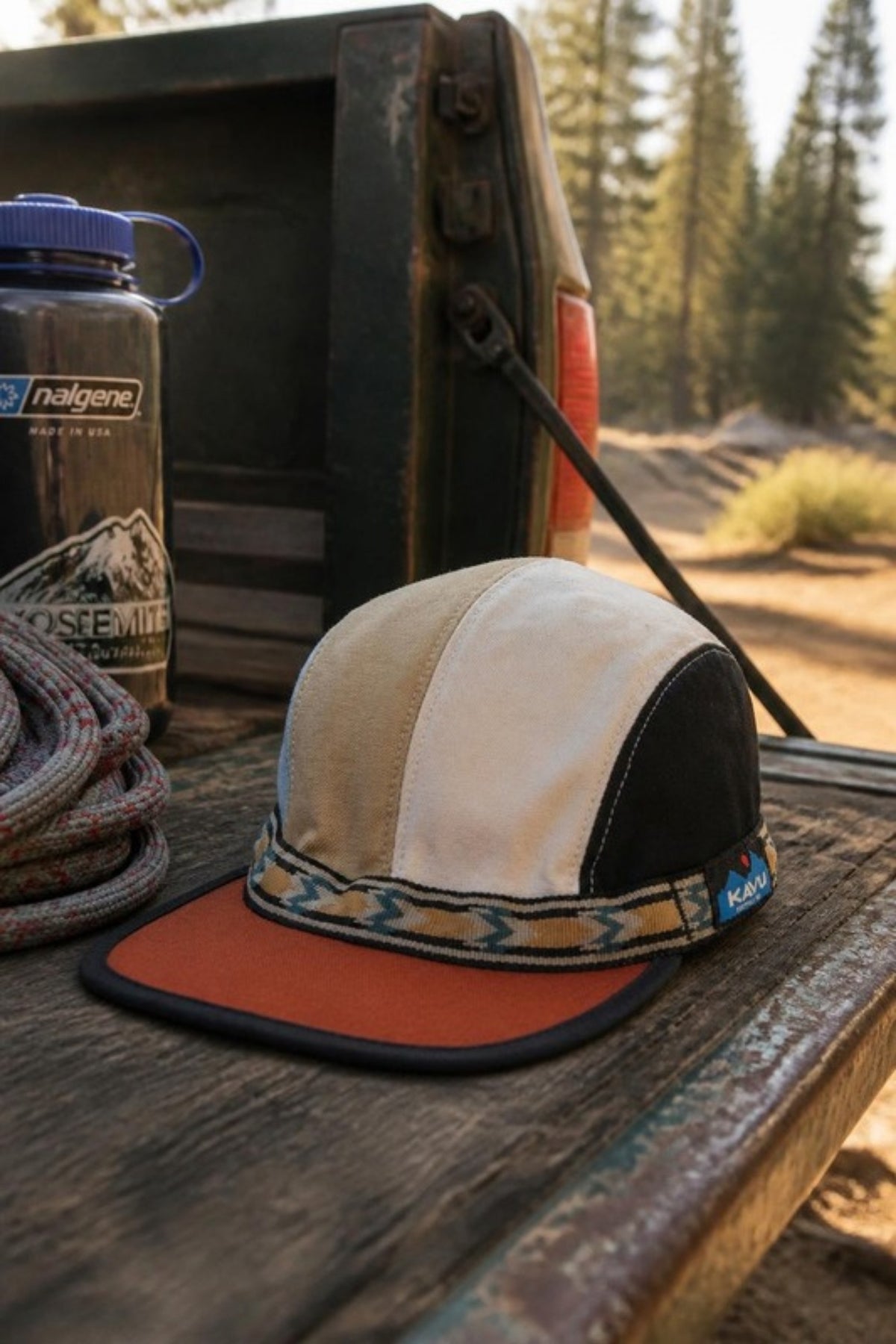 KAVU Organic Strapcap sitting on a weathered pickup tailgate at a dirt trailhead with rope and a water bottle. An easygoing strapback camp hat for road trips, trailheads and weekend adventures.