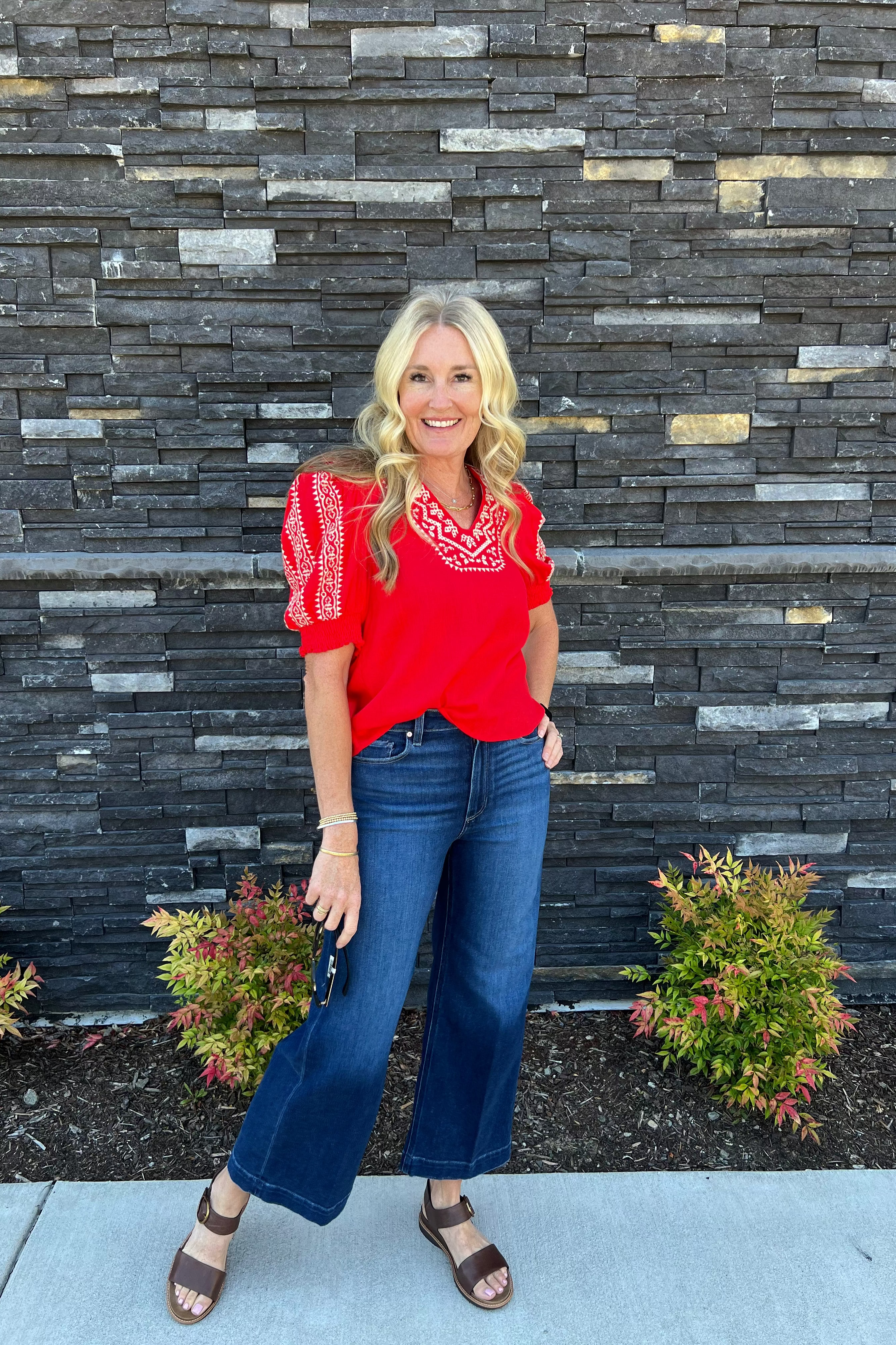 This charming embroidered smocked sleeve top features a vivid red hue, detailed embroidery on the neckline and shoulders, an ideal length, and a flattering V-neck design.