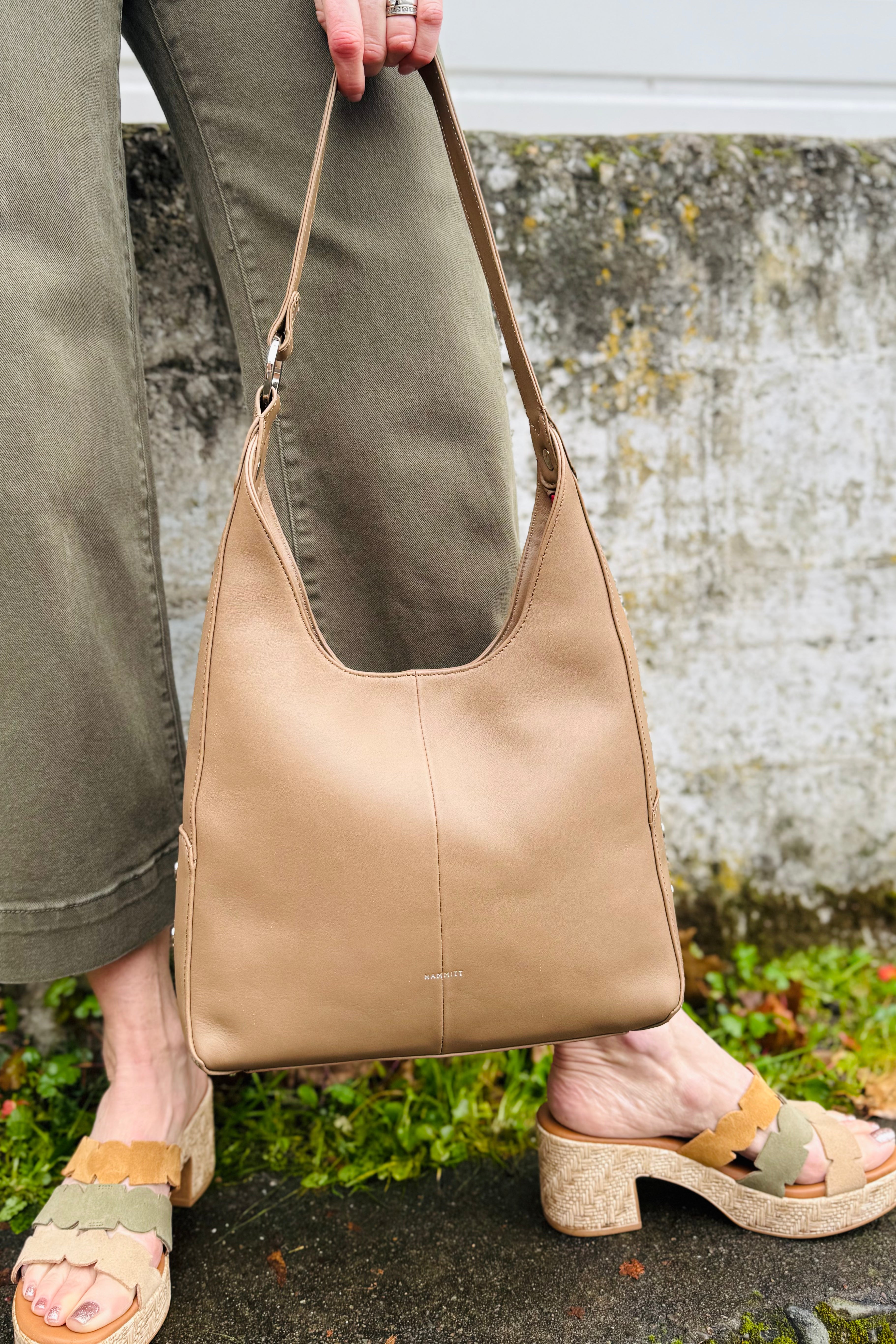 Person holding a beige leather handbag with green pants and sandals in an outdoor setting. Arktana vibe with this leather Bag.