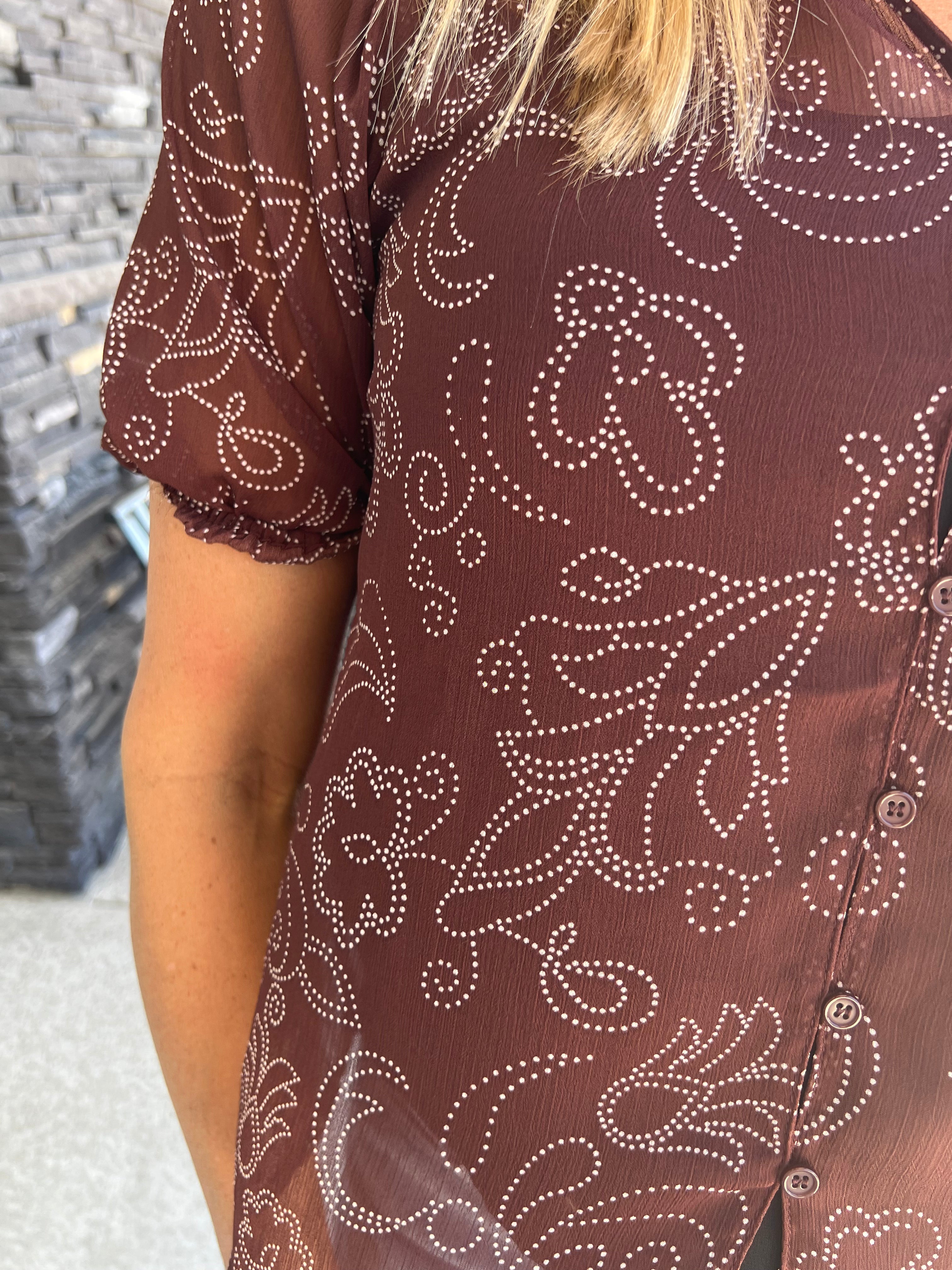 The Keep Me Close Blouse features a banded collar and short sleeves for a breezy, relaxed fit. Crafted from 100% lyocell, it offers a soft, breathable feel with a distinctive brown patterned design that complements a bohemian style. This button-down blouse is easy to care for—simply hand wash cold and hang to dry to maintain its quality and shape. Ideal for effortless, stylish comfort in warm weather.