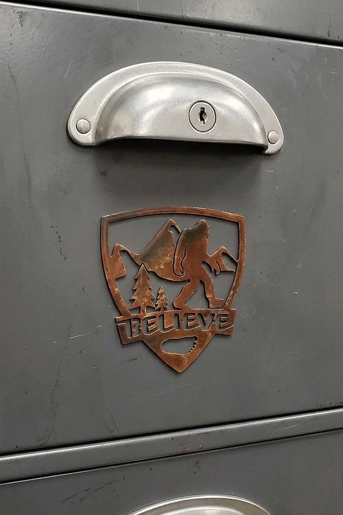 Paradise Cay Publications Bigfoot in Shield Believe magnet on a steel cabinet drawer, a rustic Bigfoot magnet for the shop, office or garage