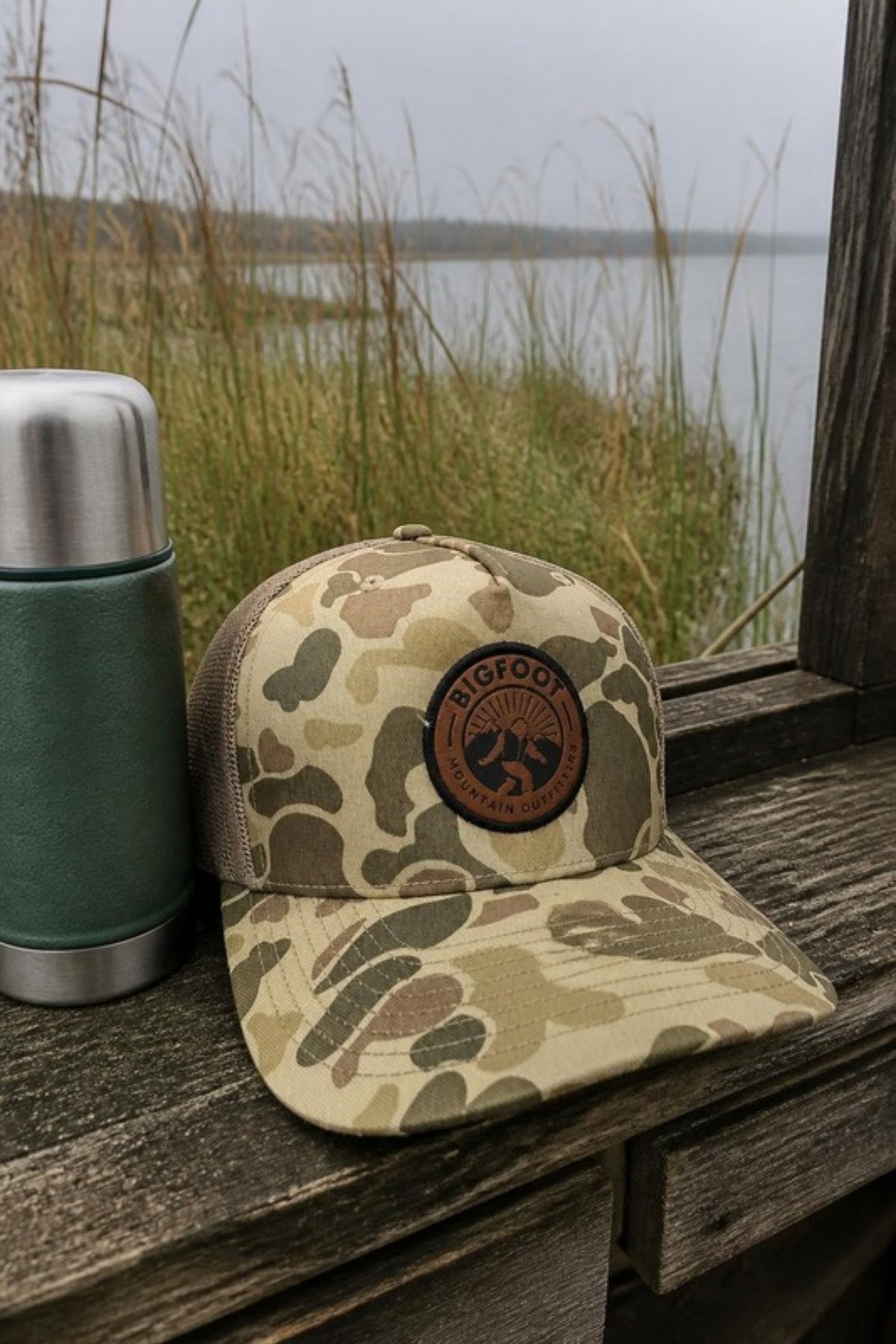 Bigfoot Mountain Outfitters BMO Mesh Hat in Harvest Duck Camo in a duck blind by the marsh, a camo leather-patch trucker hat for hunting season, fishing trips and weekends outdoors
