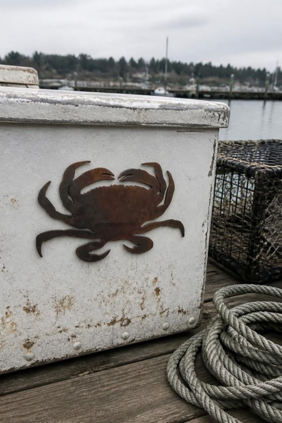 Paradise Cay Publications Dungeness crab magnet on a boat cooler at the marina next to a crab pot, a stone-tumbled laser cut steel crab magnet for the fridge, boat or beach house, and a great gift for crabbers