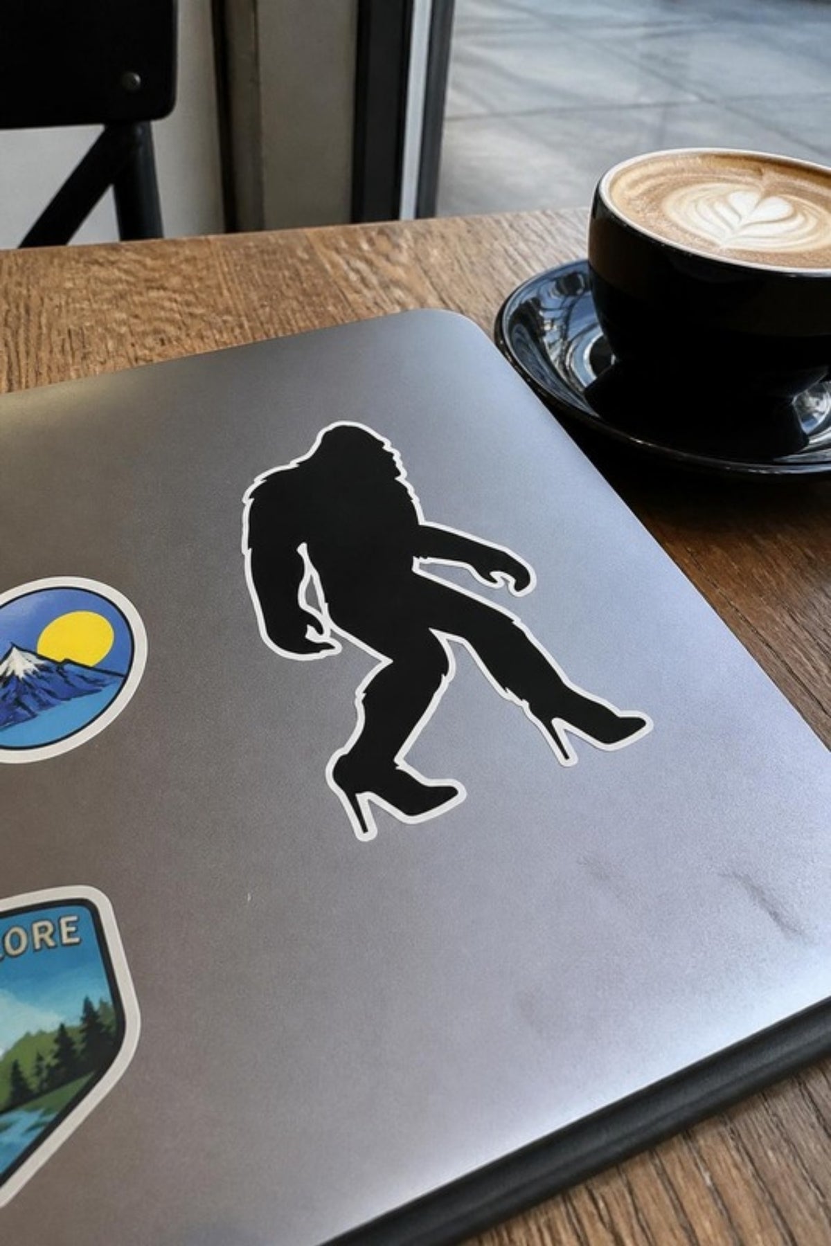 Paradise Cay Publications Sassy-Squatch sticker on a laptop at a coffee shop, a funny Bigfoot-in-heels vinyl sticker for laptops, water bottles, coolers and car windows