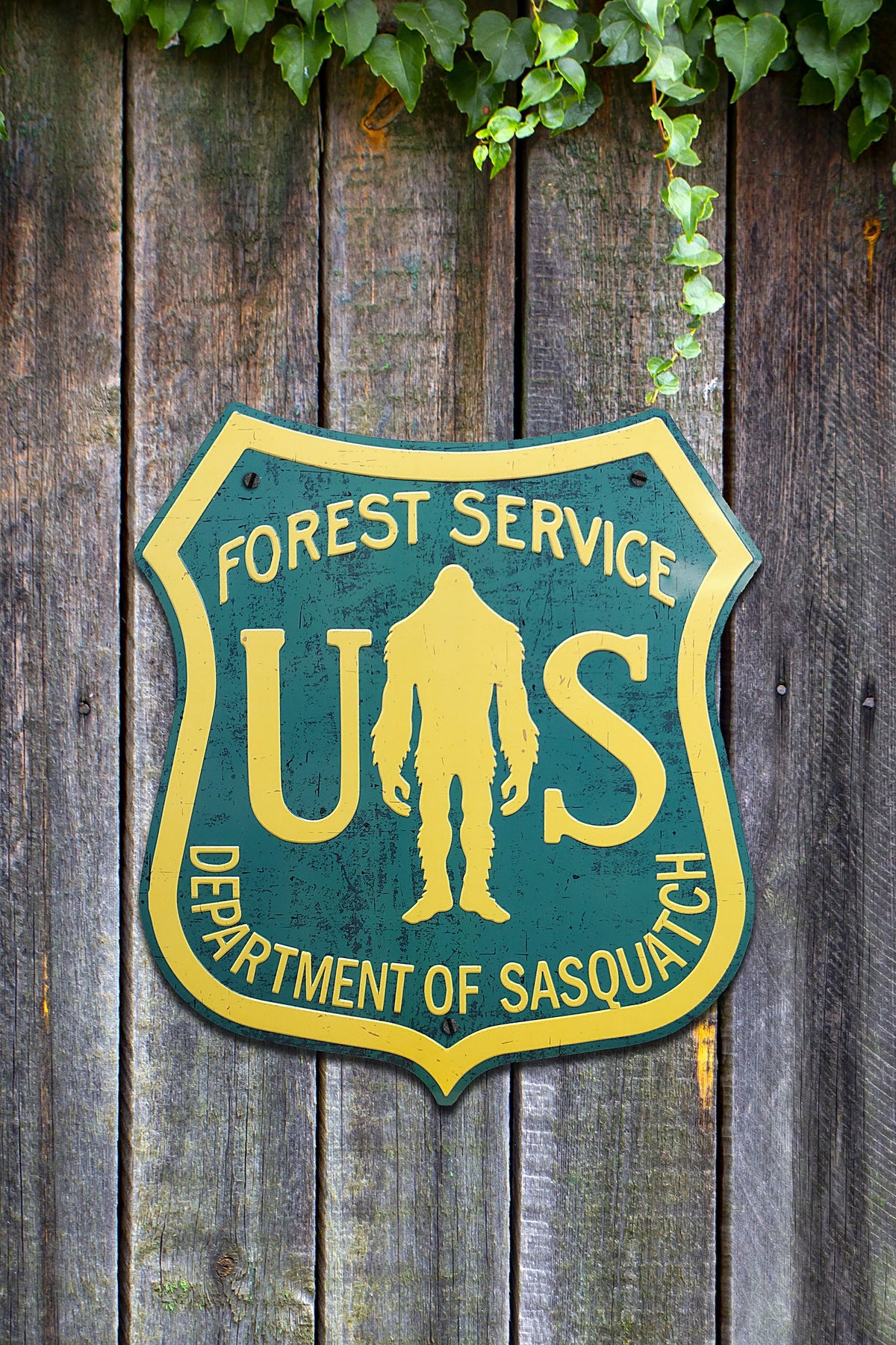Paradise Cay Publications USFS Dept of Sasquatch road sign hung on a weathered wood fence, a fun Bigfoot sign for the backyard, shop or cabin