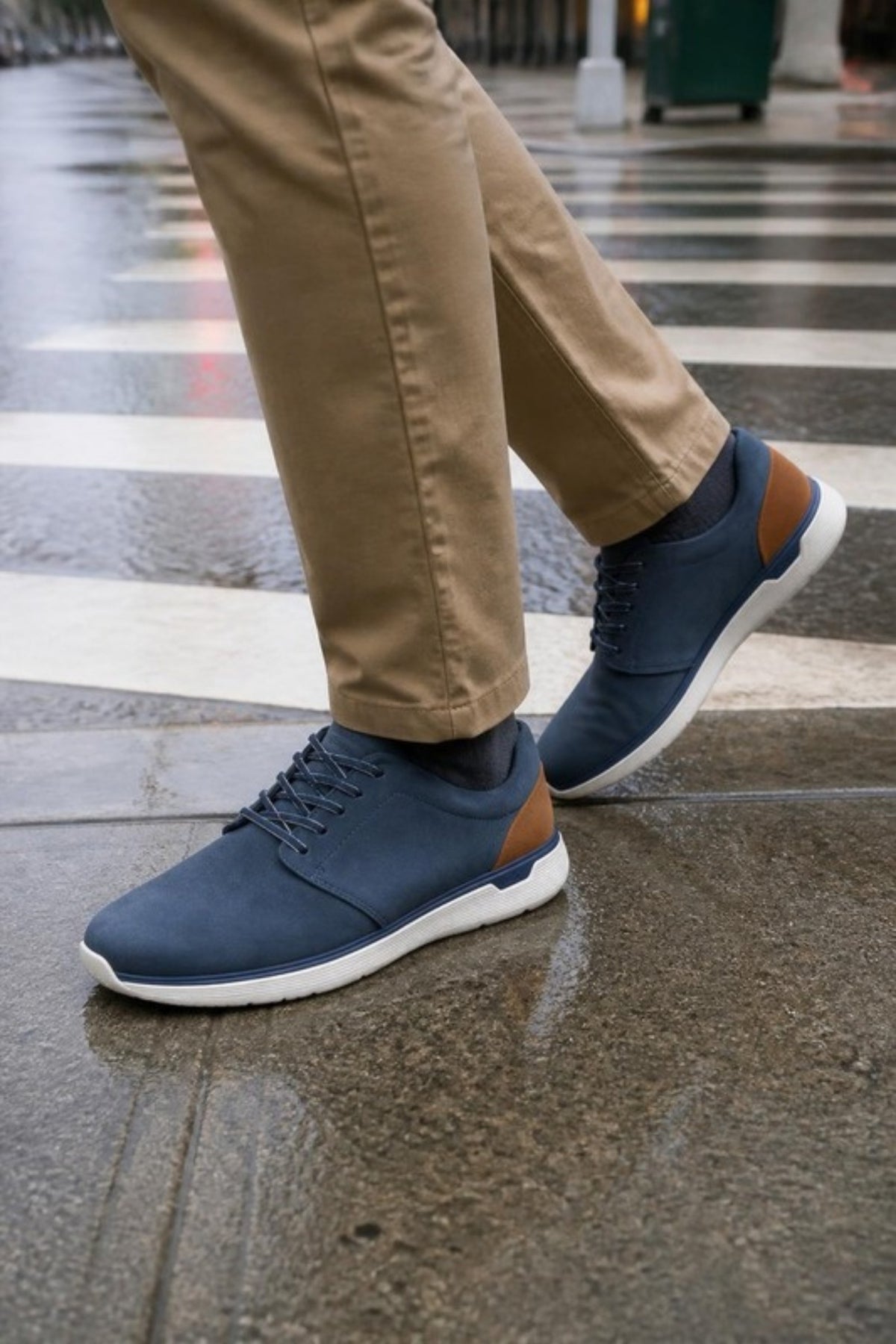 Johnston & Murphy XC4 Prentiss 2 in Navy waterproof leather with a tan heel accent and cushioned white sole, worn with khaki chinos on a rainy city crosswalk, a seam-sealed waterproof sneaker for wet PNW commutes, travel days, the office and weekend errands